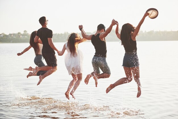 Счастливые друзья веселятся на пляже - Молодые люди играют в воде под открытым небом во время летних каникул.