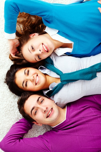 Happy friends lying down on a white carpet