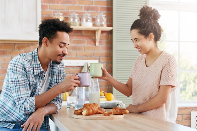 Happy friends meet together at home atmosphere, clink mugs, eat delicious croissants,