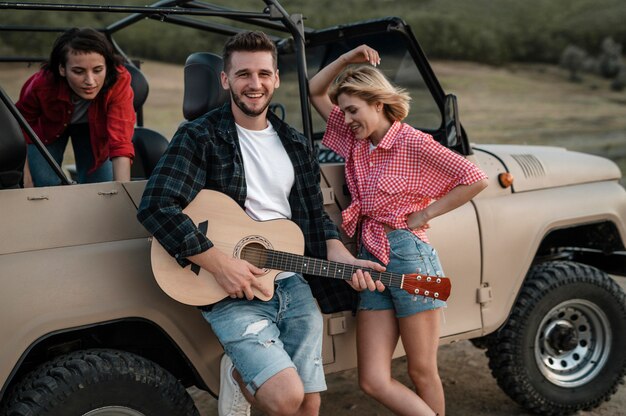 Happy friends playing guitar while traveling by car
