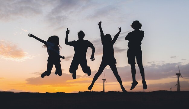 夕日にジャンプする幸せな友達のシルエット