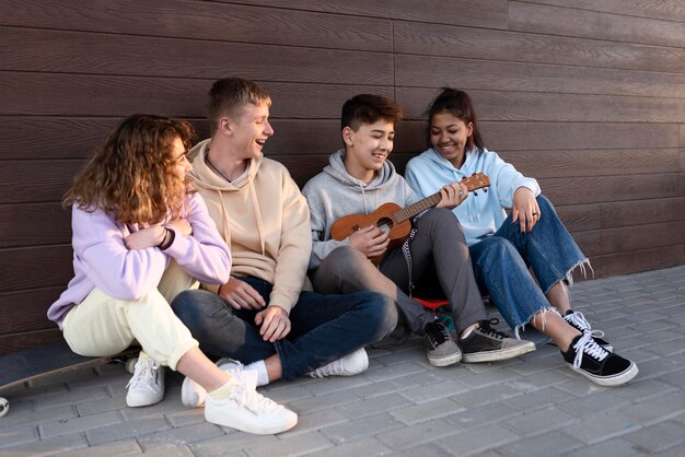 Happy friends sitting outdoors with ukulele