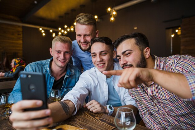 Happy friends sitting in restaurant taking selfie