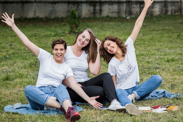 Free photo happy friends smiling sitting on park lawn