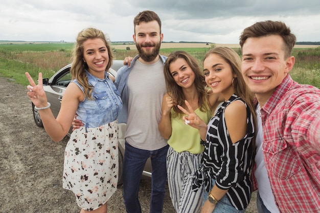 Amici felici in piedi vicino all'automobile prendendo selfie