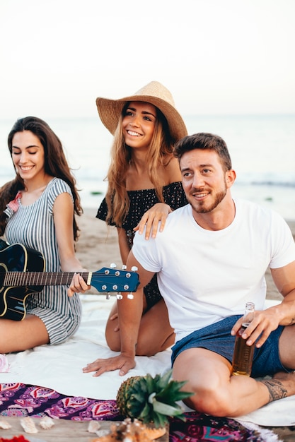 Happy friends with guitar sitting at the beach