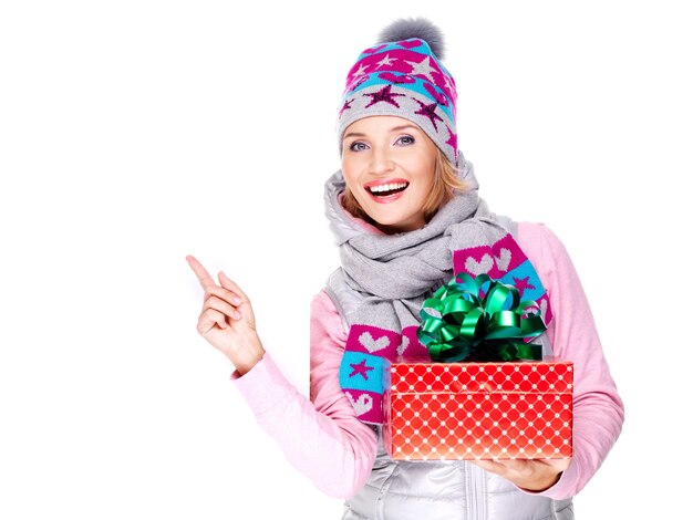 счастливая веселая женщина с подарком в зимней верхней одежде, указывая пальцем на белом