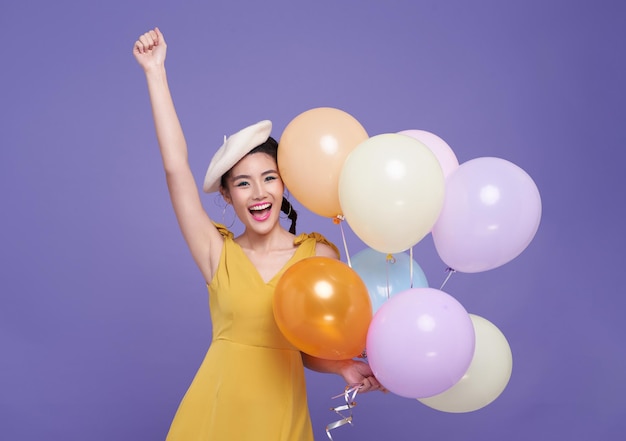 Free photo happy fun young asian woman in yellow dress celebrating holding bunch of balloons raise up hand