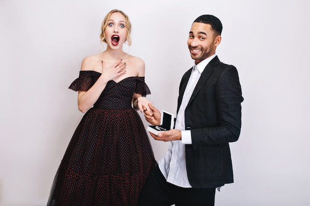 Happy funny moments of lovely cute couple celebrating Valentines day. Astonished young woman in luxury dress, handsome guy in white shirt, black jacket. Surprise, present.