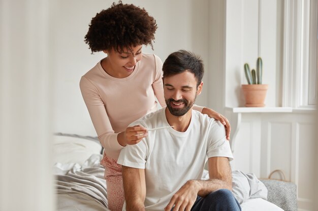 Happy future mixed race parents look positively at pregnancy test, rejoice good news in morning