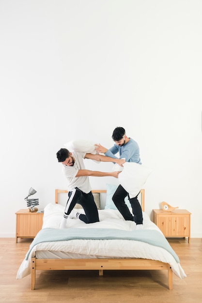 Free photo happy gay couple fighting with white pillow on bed