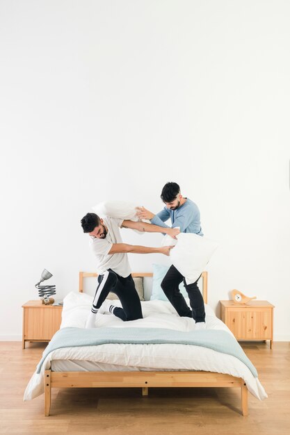 Happy gay couple fighting with white pillow on bed