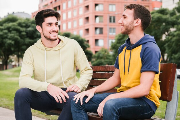 Счастливая пара геев, сидя на деревянной скамейке в парке