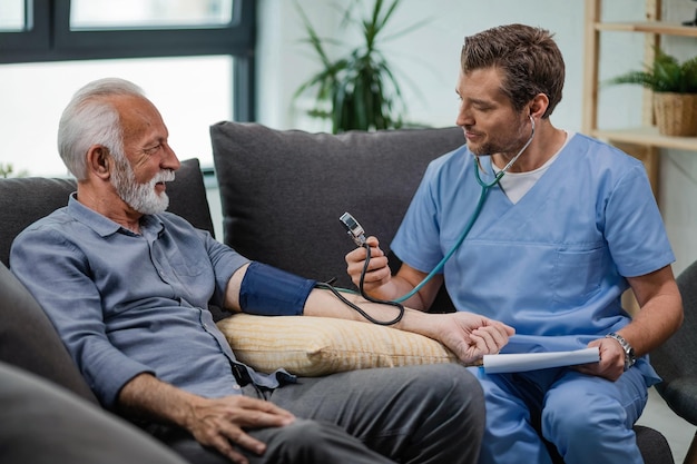 Счастливый врач общей практики измеряет артериальное давление зрелого мужчины во время визита на дом