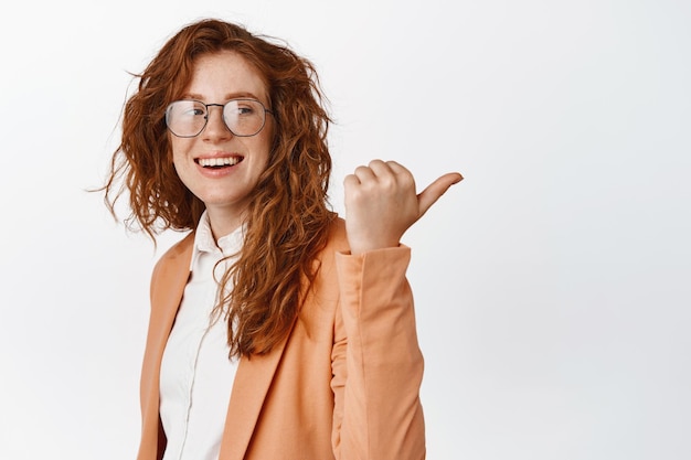 Happy ginger female entrepreneur pointing finger right and smiling showing company logo Businesswoman recommending demonstrating chart standing over white background