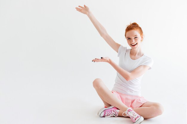 Happy ginger woman girl sitting on the floor and showing something