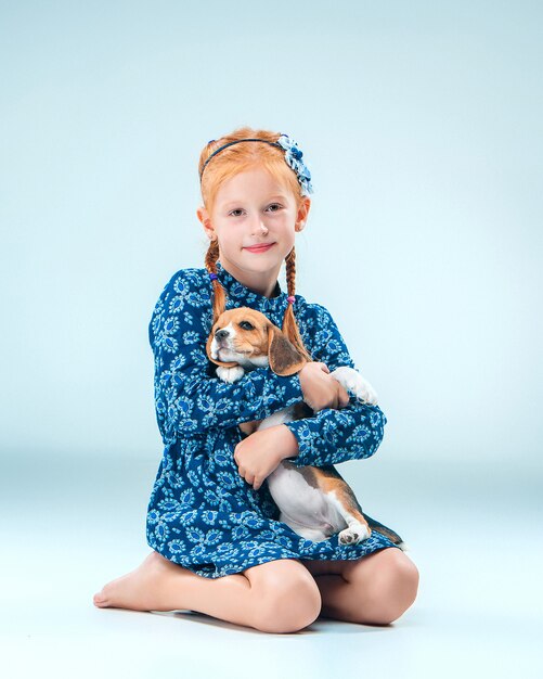 The happy girl and a beagle puppie on gray background