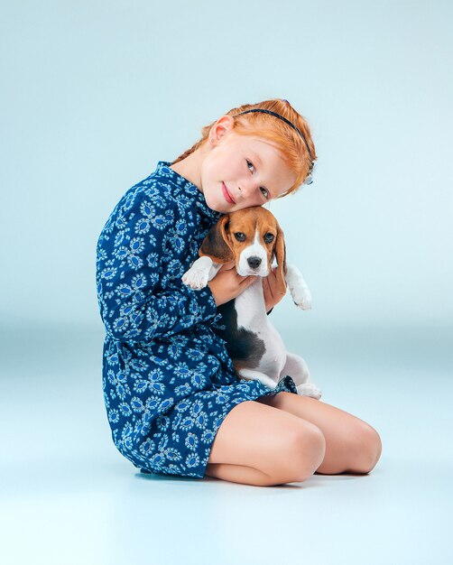 The happy girl and a beagle puppie on gray background