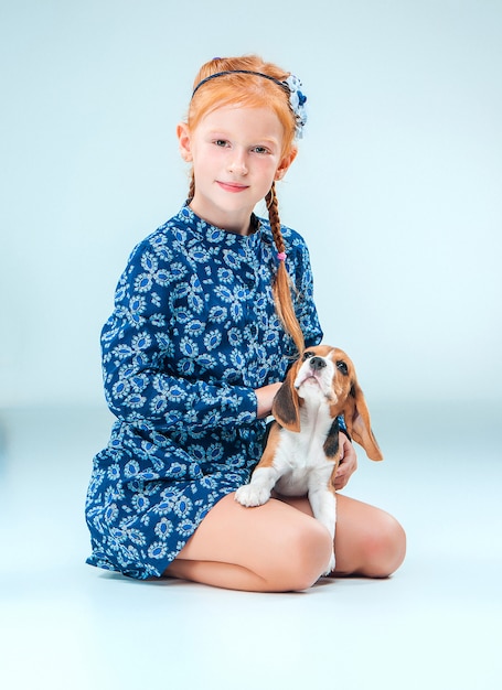 The happy girl and a beagle puppy on gray wall