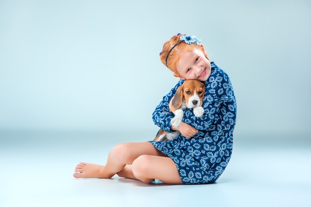 The happy girl and a beagle puppy on gray wall