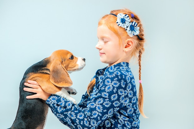 La ragazza felice e un cucciolo di beagle sulla parete grigia