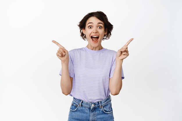 Happy girl customer young student gasping in awe pointing sideways showing two banners promo sales on two sides smiling amazed white background