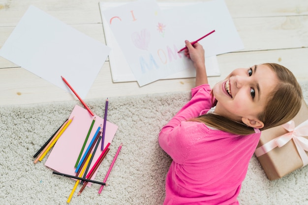 Happy girl drawing I love mom on paper 