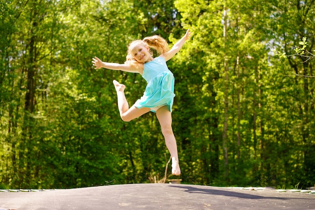 Счастливая девушка в платье прыгает на батуте в парке в солнечный летний день