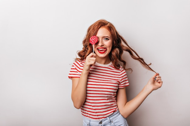 Happy girl eating candy and playing with her curly hair.  inspired ginger woman with lollipop.