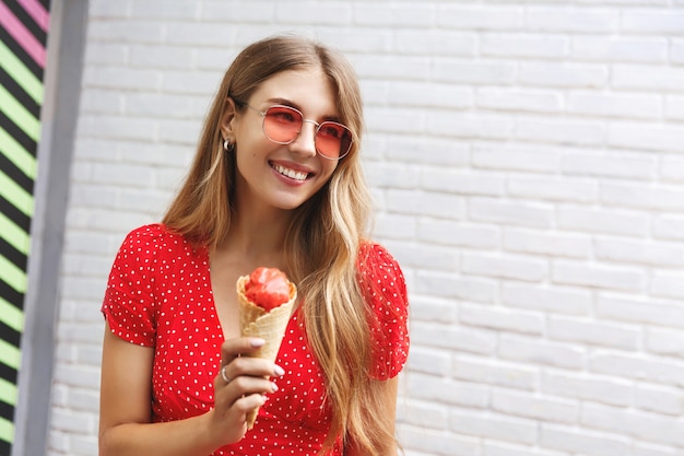 Happy girl eating ice cream on outdoor walk around city, smiling enjoying sweet street food 