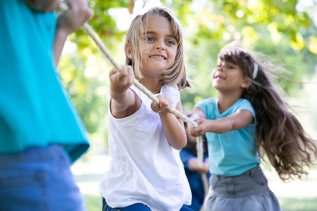 Happy girl enjoying outdoor activities, playing tug-of-war with friends. Group of children having fun in park. Childhood concept