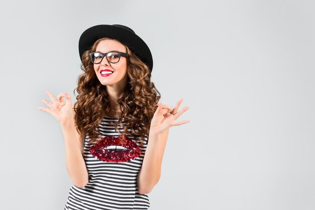 The happy girl in glasses and hat on gray wall