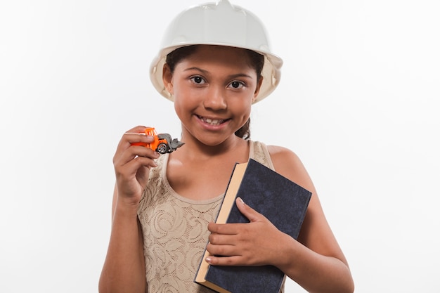 Happy girl in hardhat holding book and commercial vehicle toy