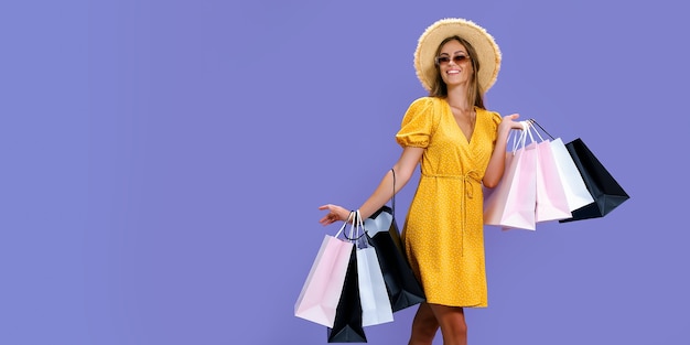 Happy girl in hat and sunglasses holds purchases on purple background black friday big sales