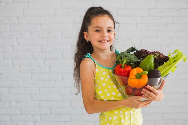 Happy girl holding colorful vegetable in glass bowl