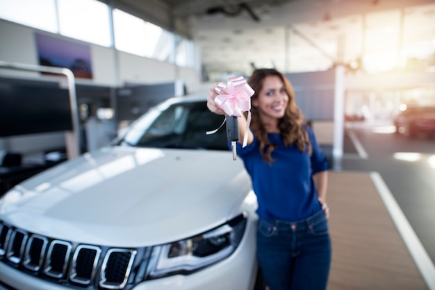 Ragazza felice che tiene le chiavi del suo suv nuovo di zecca presso lo showroom del concessionario auto