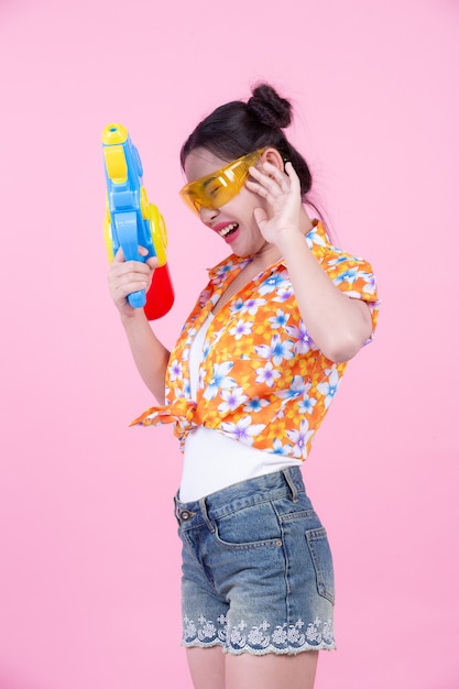 Free photo happy girl holding a pink background water gun.