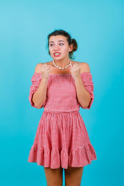 Happy girl is looking left by holding fists near chest on blue background