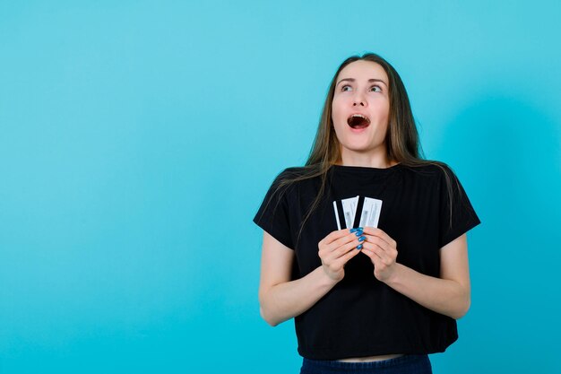 Happy girl is looking up by holding credit cards on blue background