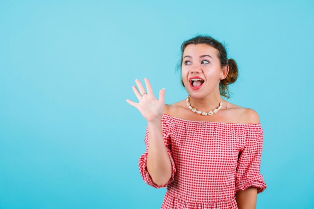 Happy girl is looking up by showing hi gesture with hand on blue background