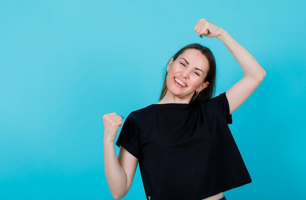 Happy girl is raising up her fists on blue background