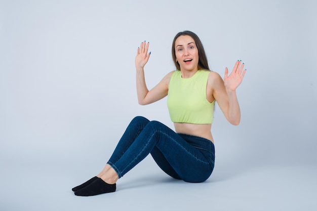 Free photo happy girl is raising up her hands by sitting on floor on white background