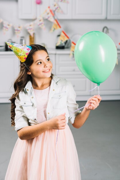 Happy girl looking at green balloon in kitchen