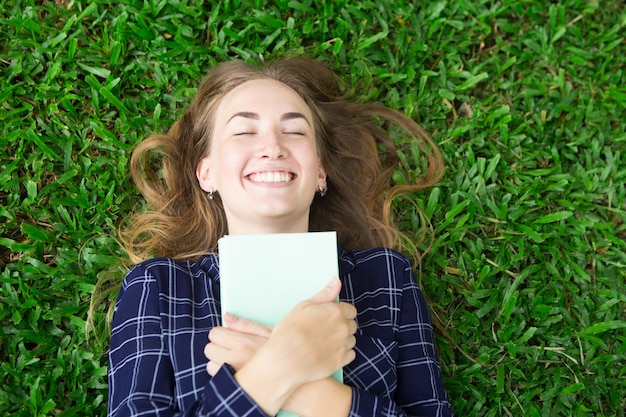 Free photo happy girl lying on grass and embracing book