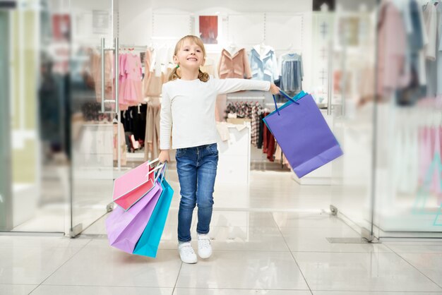 多くのバッグを持つショッピングセンターでポーズをとって幸せな女の子。