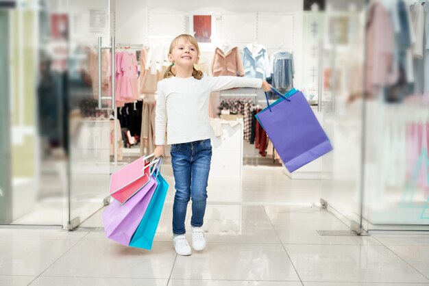 Happy girl posing in shopping centre with many bags.