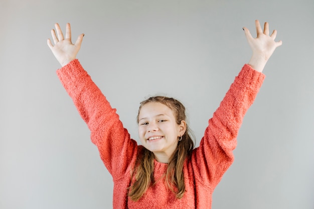 Happy girl raising her arms on grey background