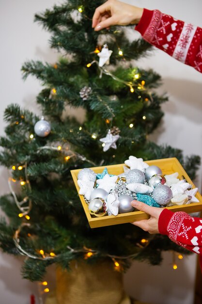 Premium Photo | A Happy Girl In A Red Sweater Holds A Tray Of Christmas Toys And Decorates The Christmas Tree At Home For Christmas, 2022 Year Of The Tiger. Side View.