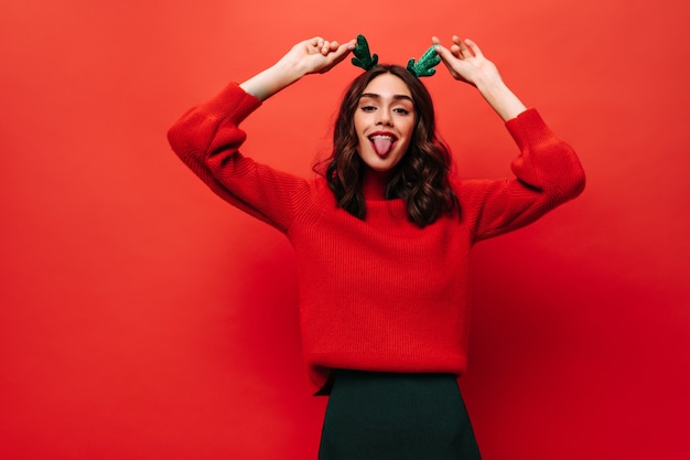 孤立した壁に舌を示す赤いセーターの幸せな女の子