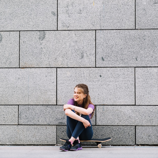 행복 한 여자는 벽돌 벽 앞에서 스케이트 보드에 앉아